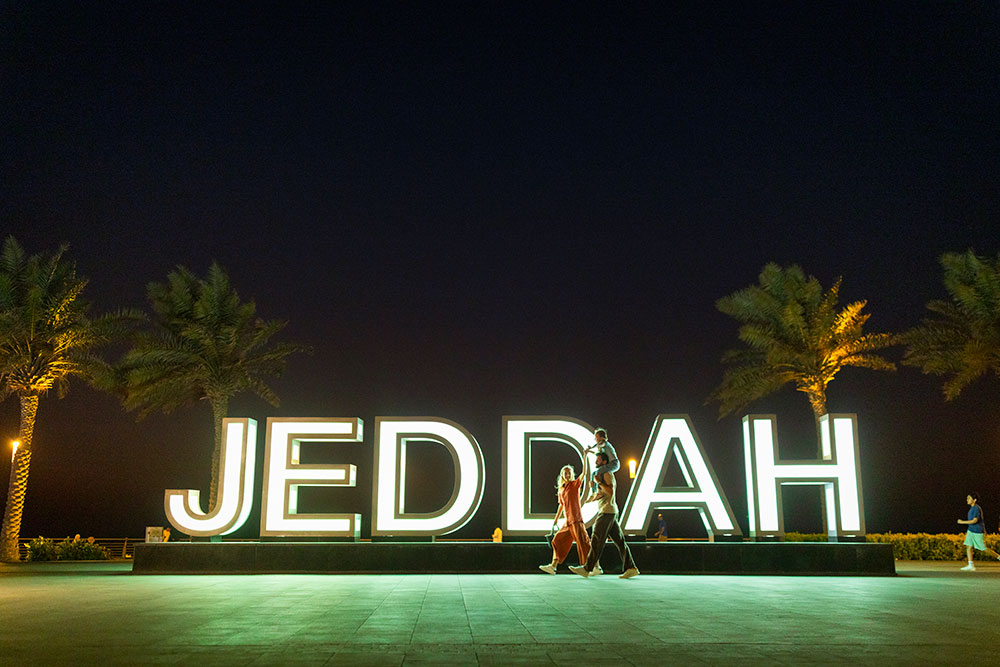 Familie spaziert nachts am Jeddah-Schriftzug vorbei